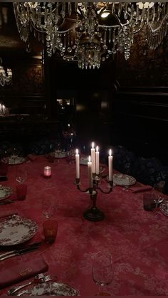 a dining room table is set with place settings and lit candles in front of the chandelier