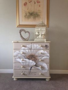 a white dresser with flowers painted on it and a birdcage next to it