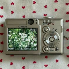 a digital camera sitting on top of a bed next to a red and white blanket