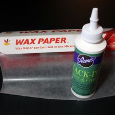 a bottle of wax paper sitting on top of a piece of clear plastic next to a tube of glue