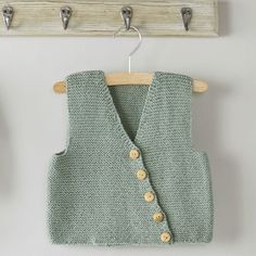 a knitted vest hanging on a wooden coat rack with hooks and clothes pins attached to it