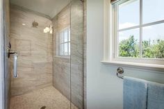 a walk in shower next to a window with a towel hanging on the wall and a light fixture