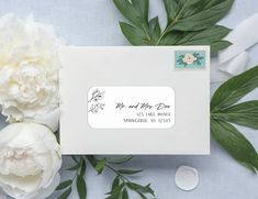 a white envelope with a stamp on it next to some flowers and green leafy branches