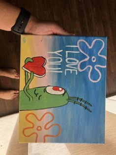 a person holding up a painting with an image of a frog on it's back