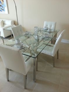 a glass dining table with white chairs and plates on it in a living room area