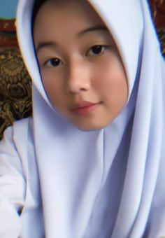 a young woman wearing a white hijab looking at the camera with an intense look on her face