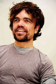 a man with long hair and beard smiling at the camera while wearing a gray t - shirt