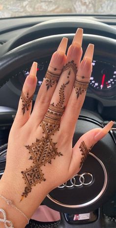 a woman's hand with henna tattoos on her left wrist and the steering wheel behind her