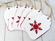 four white tags with red snowflakes hanging from twine on wood flooring