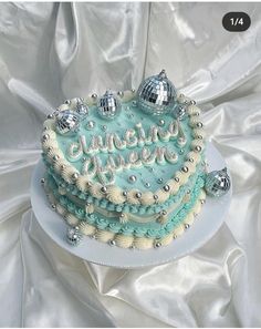 a cake that is sitting on top of a white plate with blue frosting and silver decorations