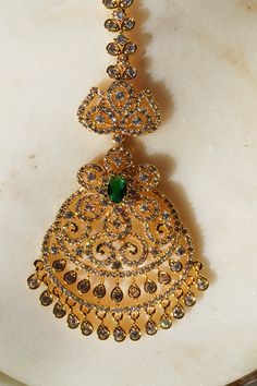 Enhance your traditional allure with the 'Jirisa - Gold AD Maang Tikka.' This exquisite piece, measuring approximately 5.51 inches in height and 1.77 inches in width, is available in two stunning options: Gold and Green, and Gold and Ruby-Green, each adding a touch of elegance to complement your style. The Gold and Green variant delicately features small teardrop-shaped stones dangling from the base, offering a subtle yet captivating charm to your appearance. Alternatively, the Gold and Ruby-Gre Elegant Green Chandbalis For Eid, Elegant Chandbalis For Eid Ceremonies, Elegant Green Tikka For Festive Occasions, Elegant Green Tikka For Festive Season, Elegant Ceremonial Tikka For Eid, Elegant Ceremonial Tikka For Diwali, Green Bollywood Tikka With Intricate Design, Elegant Green Tikka With Tilla Detail, Green Intricate Design Tikka For Festivals