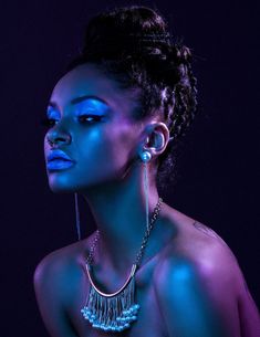 a woman with blue light on her face and necklaces around her neck, posing for the camera