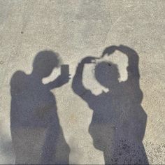 two people standing next to each other with their shadows on the ground and one person taking a photo