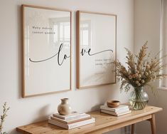 two framed pictures on the wall above a wooden table with flowers and books in vases