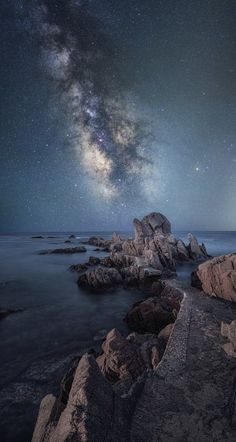 the night sky is filled with stars and clouds above rocks in the ocean, as well as milky