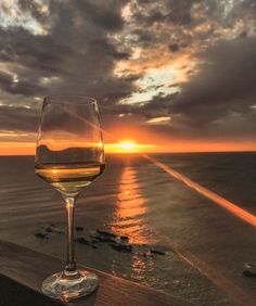 a glass of white wine sitting on top of a wooden table next to the ocean