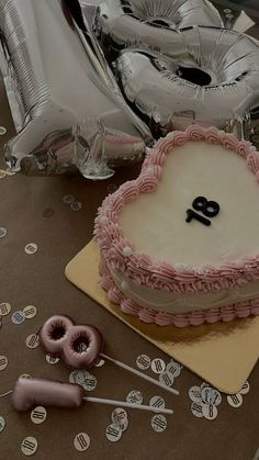 a birthday cake on a table with balloons and confetti in the shape of a heart