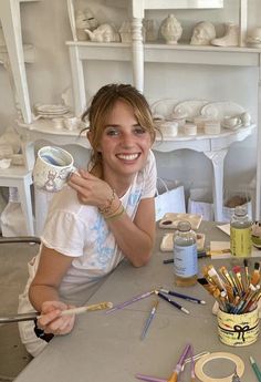 a woman sitting at a table with paint and brushes in front of her, smiling