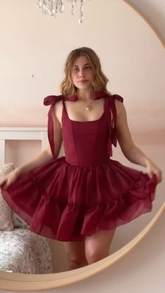 a woman wearing a red dress standing in front of a mirror with her hands on her hips