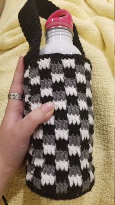 a hand holding a black and white crocheted water bottle cover