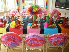 the table is set with colorful paper flowers and napkins on top of each chair