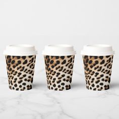 three leopard print coffee cups sitting on top of a white marble counter with one cup in the middle