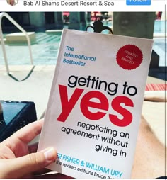 someone holding up a book about getting to yes in front of an outdoor swimming pool