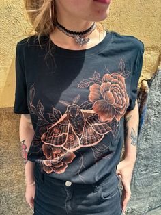 a woman standing in front of a yellow wall wearing a black shirt with flowers on it