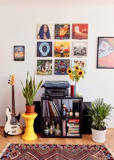 there are many pictures on the wall above the bookshelf and guitar in the room