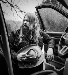 a man with long hair wearing a cowboy hat sitting in the driver's seat of a truck