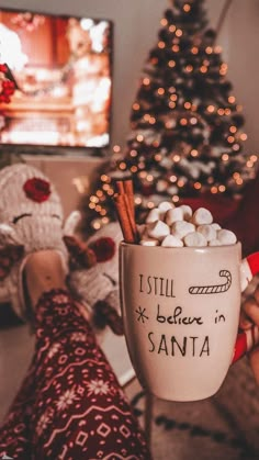 someone holding up a mug with cinnamon sticks in it and the words still believe in santa written on it