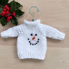 a knitted snowman sweater ornament next to holly