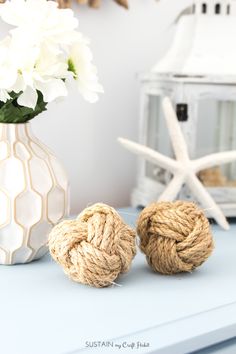 two balls of rope sitting on top of a blue table next to a vase with white flowers