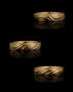 three gold wedding bands with wavy shapes on black background, one in the middle and one in