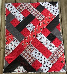 a red and black quilt with mickey mouses on the front is laying on a wooden floor