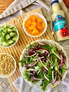 a wooden table topped with bowls of salad and condiments next to bottles of dressing