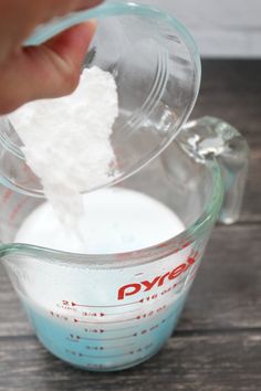 someone is adding sugar to a measuring cup filled with water and flour on a wooden table