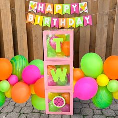 a birthday decoration with balloons and streamers on the side of a wooden fence that reads happy birthday tw