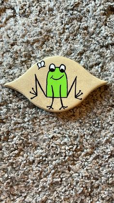 a wooden brooch with a green frog on it's back sitting on carpet