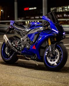 a blue motorcycle parked in a parking lot next to a building at night with its lights on