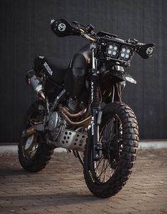 a black motorcycle parked on top of a brick floor next to a wall and door