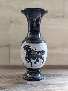 a black and white vase sitting on top of a wooden table next to a wall