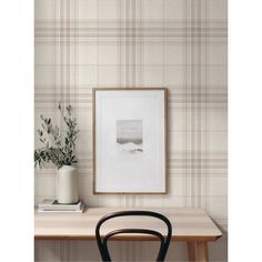 a table with a chair, vase and plant on it in front of a plaid wallpaper