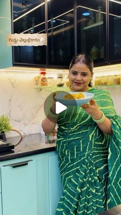 a woman in a green sari is holding a plate with some food on it