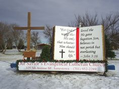 a large sign in the snow with a wooden cross behind it that says, our savor's evangetal lutherian church