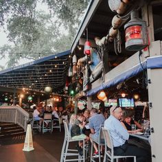 many people are sitting at tables in front of a bar with lights hanging from the ceiling