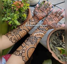 two hands with henna designs on them and some potted plants in the background