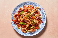 a blue and white plate filled with shrimp, peppers, and carrots on top of a table