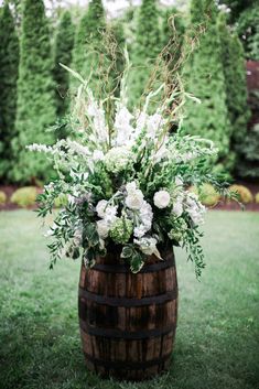 a wooden barrel with white flowers and greenery in it sitting on the grass outside