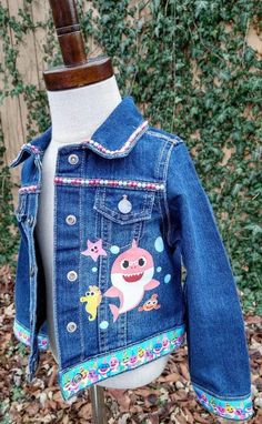 This Baby Shark Denim Jacket is perfect for your little one! Constructed from lightweight denim and detailed with Baby Shark characters, it makes a fun and stylish addition to any wardrobe. With its added ribbon detail, it's sure to be a hit with the little ones. These jackets run TRUE TO SIZE. Please note that jackets are personalized and made to order. They will not always be exact replicas. Denim color may vary. Playful Cotton Denim Jacket With Pockets, Blue Cotton Denim Jacket For Playtime, Playtime Denim Jacket With Pockets, Cute Cotton Denim Jacket, Cute Fitted Blue Denim Jacket, Cute Medium Wash Denim Jacket, Playful Long Sleeve Cotton Denim Jacket, Playful Denim Jacket For Fall, Long Sleeve Denim Jacket For Playtime